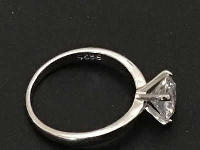 Sale Photo Thumbnail #219: A sterling silver solitaire ring featuring a large round brilliant cut clear stone (likely cubic zirconia or simulated diamond) in a four-prong setting. The interior band is stamped "S925". Shown on a ring mandrel as a size 6. In good pre-owned condition 