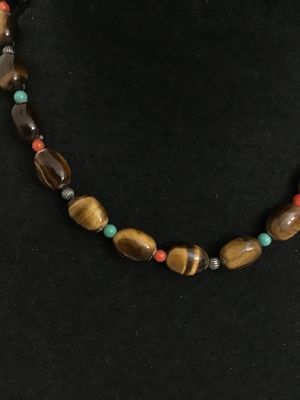 Sale Photo Thumbnail #21: A beaded gemstone necklace featuring smooth, polished tiger's eye oval beads accented with small turquoise and red/coral-tone spacer beads and silver-tone fluted metal spacers. Finished with a decorative silver-tone toggle closure clasp. In good pre-owned