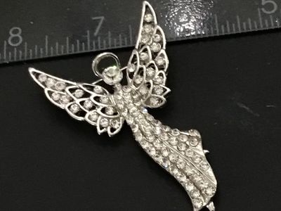 Sale Photo Thumbnail #223: Silver-tone metal brooch designed in the shape of a winged guardian angel with a halo, densely set with clear rhinestones throughout the body and openwork wings. Features a standard pin back with rollover safety clasp. Measures approximately 2.25 inches i