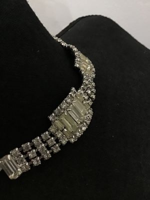 Sale Photo Thumbnail #290: Vintage silver-tone rhinestone choker necklace featuring a central panel of baguette and round-cut clear stones, flanked by multi-strand detail and dangling baguette accents. Features an adjustable hook clasp with extension tail. Shows minor light age-app