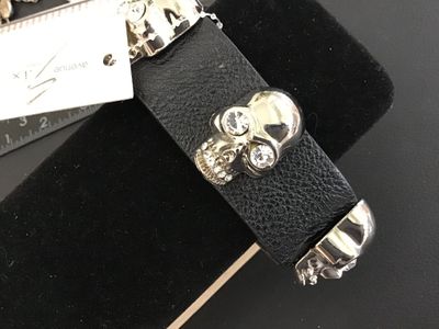 Sale Photo Thumbnail #57: Avenue Six Collection black textured leather or faux-leather cuff bracelet featuring three silver-tone metallic skulls set with clear rhinestone eyes and teeth accents. Secured with double snap closure. Measures approximately 8.5 to 9 inches long total. I