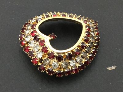 Sale Photo Thumbnail #160: A vintage gold-tone heart-shaped brooch pin encrusted with red and clear/smokey rhinestones set in prong settings. Features a rollover safety clasp on the back. Measures approximately 1.5 inches wide by 1.5 inches tall. Overall good vintage condition with