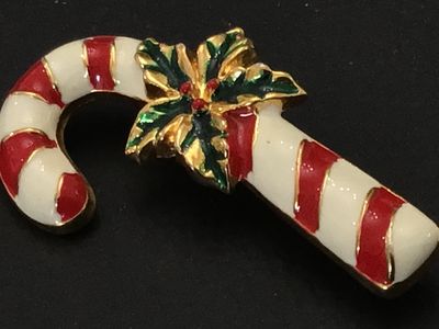 Sale Photo Thumbnail #215: A festive gold-tone holiday brooch featuring a candy cane motif with red and white enamel detailing, accented by green and red enamel holly leaves and berries at the center. Standard pin stem with safety clasp on back. Measures approximately 2 inches long