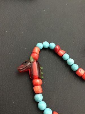 Sale Photo Thumbnail #3: Unique beaded strand necklace featuring turquoise-colored and red coral-tone beads interspersed with blown/cast glass horse head charms. Features a focal drop with a glass horse head, large red bead, and a stamped metal cross pendant. Includes a metal tog