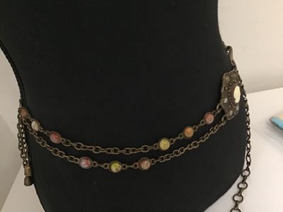 Sale Photo Thumbnail #260: A vintage brass-tone chain belt featuring a central ornate pendant set with a portrait cameo insert and surrounding multi-color cabochon accents. The chain strand includes additional bezel-set multi-colored faux stones and a hook clasp closure with decora