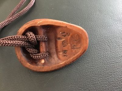 Sale Photo Thumbnail #17: Hand-carved wooden pendant depicting a smiling traditional Korean Hahoe mask (Yangban or Hahoe mask style). Mounted on a braided brown cord. Features characters/marking carved on the reverse side. Shows light vintage wear with a smooth finish.