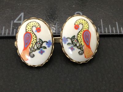 Sale Photo Thumbnail #198: A vintage double-oval brooch featuring hand-painted or transfer porcelain cabochons set in gold-tone metal. Each oval displays a colorful bird perched on a floral branch. Measures approximately 1.25 inches across. The pin back and C-clasp are in functiona