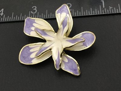 Sale Photo Thumbnail #97: A floral brooch featuring layered petals in light purple and white enamel with gold-tone edging. The back shows a textured gold-tone finish with a standard pin stem and rollover safety clasp. Measures approximately 2.25 inches across. Overall good pre-own