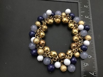 Sale Photo Thumbnail #271: A chunky gold-tone link bracelet featuring an array of dangling bead charms including textured gold-tone metal spheres, smooth dark blue beads, translucent greyish-blue beads, and white beads. The bracelet measures approximately 7 inches in circumference.