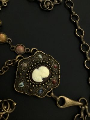Sale Photo Thumbnail #258: A vintage brass-tone chain belt featuring a central ornate pendant set with a portrait cameo insert and surrounding multi-color cabochon accents. The chain strand includes additional bezel-set multi-colored faux stones and a hook clasp closure with decora