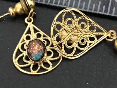 Sale Photo Thumbnail #245: A pair of vintage gold-tone pierced drop/dangle earrings featuring intricate filigree teardrop frames. Each earring is set with an oval cabochon stone showcasing flecks of copper, blue, and brown reminiscent of dragon's breath glass or matrix stone. Earri