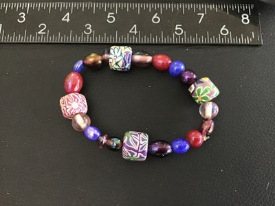 Sale Photo Thumbnail #49: Multicolor beaded stretch bracelet featuring patterned polymer clay millefiori-style focal beads alongside vibrant glass and iridescent beads in shades of purple, blue, red, and green. Measures approximately 2.5 inches in diameter resting relaxed. Good co