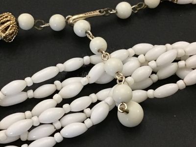 Sale Photo Thumbnail #167: Vintage multi-strand statement necklace featuring white rice/oval-shaped molded  glass beads. Finished with decorative gold-tone filigree end caps and an adjustable hook closure with extension chain. Marked 'JAPAN' on the hook clasp. In good vintage condi