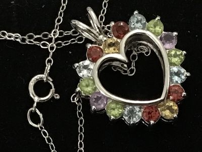 Sale Photo Thumbnail #145: A sterling silver heart-shaped pendant necklace featuring a reversible design. One side is adorned with multi-color round faceted gemstones including amethyst, peridot, citrine, garnet, and blue topaz, while the reverse side features a halo of uniform lig