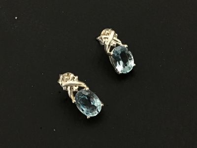 Sale Photo Thumbnail #189: Pair of  silver stud earrings featuring oval-cut light blue gemstones, likely aquamarine or blue topaz, set in four-prong settings with small decorative accents at the top. Includes matching silver friction butterfly backs. Good pre-owned condition with m