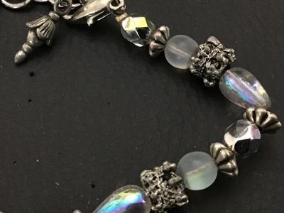 Sale Photo Thumbnail #185: Beaded bracelet featuring iridescent teardrop and faceted glass beads, frosted round beads, and ornate textured silver-tone spacer accents. Finished with a lobster claw clasp and small charm detail. In good pre-owned condition with light surface wear.