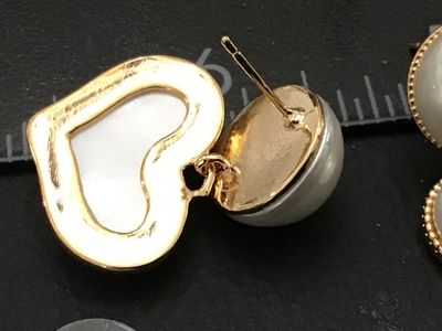 Sale Photo Thumbnail #231: Pair of gold-tone post earrings featuring round white faux pearl studs with dangling, beaded-edge heart charms filled with a matching pearlescent finish. Includes plastic clutch backs. Condition is very good with light surface wear.
