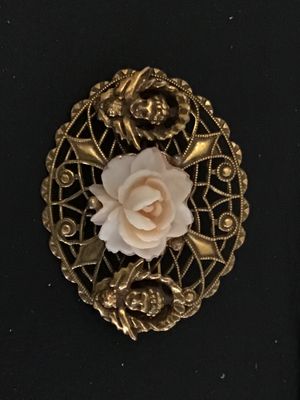 Sale Photo Thumbnail #41: An intricate oval vintage brooch featuring detailed gold-tone filigree metalwork, a central carved faux-coral or resin rose bloom, and two cherub/putti figures on either side. Features a rollover safety clasp on the reverse. Shows minor signs of vintage w