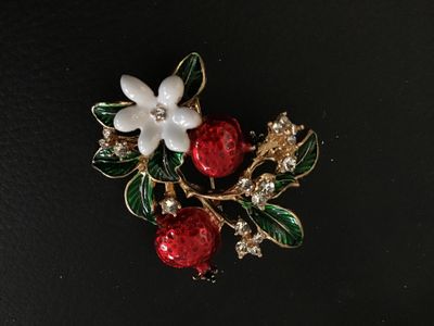 Sale Photo Thumbnail #76: Gold-tone floral brooch featuring red enamel pomegranates, green enamel leaves, a white flower, and clear rhinestone accents. Includes a standard pin back with locking clasp. In good pre-owned condition with no missing stones observed.