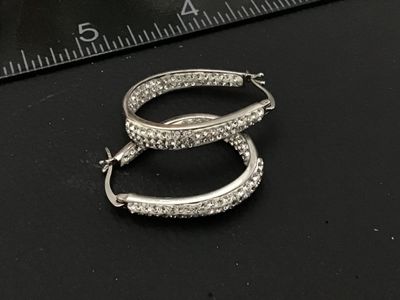 Sale Photo Thumbnail #92: Pair of silver-tone oval hoop earrings set with clear pavé rhinestones/crystals. Features latch-back closures. Earrings measure approximately 1 inch in length as shown against the scale. Good pre-owned condition with all stones intact.