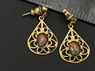 Sale Photo Thumbnail #246: A pair of vintage gold-tone pierced drop/dangle earrings featuring intricate filigree teardrop frames. Each earring is set with an oval cabochon stone showcasing flecks of copper, blue, and brown reminiscent of dragon's breath glass or matrix stone. Earri