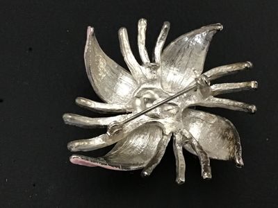 Sale Photo Thumbnail #180: Vintage silver-tone metal floral brooch featuring three blue dimensional rose buds at the center, surrounded by pale pink enamel leaves and textured silver-tone tendrils/stems. Secured with a standard rollover safety clasp on the back. Shows minor enamel 