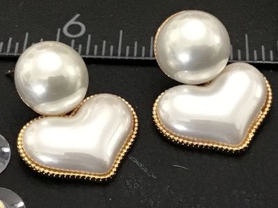 Sale Photo Thumbnail #229: Pair of gold-tone post earrings featuring round white faux pearl studs with dangling, beaded-edge heart charms filled with a matching pearlescent finish. Includes plastic clutch backs. Condition is very good with light surface wear.