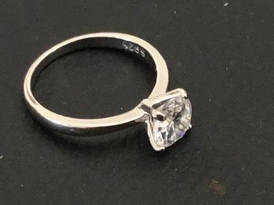 Sale Photo Thumbnail #218: A sterling silver solitaire ring featuring a large round brilliant cut clear stone (likely cubic zirconia or simulated diamond) in a four-prong setting. The interior band is stamped "S925". Shown on a ring mandrel as a size 6. In good pre-owned condition 