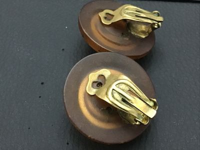 Sale Photo Thumbnail #283: Pair of vintage round clip-on earrings featuring large faceted amber-colored glass or lucite center stones set in dark brown wooden frames detailed with carved star motifs. Equipped with gold-tone clip-on backs. Each earring measures approximately 1.25 in