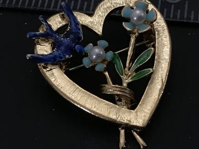Sale Photo Thumbnail #111: Vintage gold-tone openwork heart brooch featuring a blue enamel bird, enamel flowers with faux pearl centers, and green leaf accents. Features textured gold-tone finish on the front and a standard pin back with rollover clasp. Measures approximately 1.25 