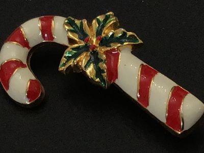 Sale Photo Thumbnail #214: A festive gold-tone holiday brooch featuring a candy cane motif with red and white enamel detailing, accented by green and red enamel holly leaves and berries at the center. Standard pin stem with safety clasp on back. Measures approximately 2 inches long