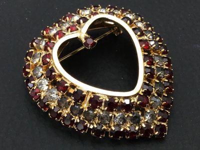 Sale Photo Thumbnail #159: A vintage gold-tone heart-shaped brooch pin encrusted with red and clear/smokey rhinestones set in prong settings. Features a rollover safety clasp on the back. Measures approximately 1.5 inches wide by 1.5 inches tall. Overall good vintage condition with