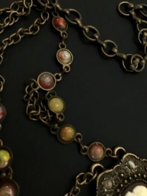 Sale Photo Thumbnail #261: A vintage brass-tone chain belt featuring a central ornate pendant set with a portrait cameo insert and surrounding multi-color cabochon accents. The chain strand includes additional bezel-set multi-colored faux stones and a hook clasp closure with decora