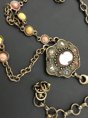 Sale Photo Thumbnail #257: A vintage brass-tone chain belt featuring a central ornate pendant set with a portrait cameo insert and surrounding multi-color cabochon accents. The chain strand includes additional bezel-set multi-colored faux stones and a hook clasp closure with decora