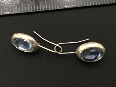 Sale Photo Thumbnail #193: Pair of wire hook drop earrings featuring oval light blue glass cabochons set in silver-tone bezels with textured backs. In good pre-owned condition with slight surface wear.