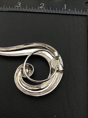 Sale Photo Thumbnail #251: A vintage silver-tone scarf clip brooch featuring an abstract swirl design with a central accent sphere. Marked 'VERA-LU' on the back mechanism. Measures approximately 3 inches in length and 1.5 inches in width. In good condition with minimal surface wear