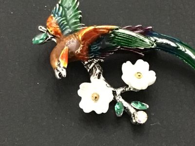 Sale Photo Thumbnail #233: Colorful enameled costume jewelry brooch featuring a long-tailed bird perched on a flowering branch. Styled with vibrant green, orange, and purple enamel, white carved flower accents, and green/clear rhinestones on silver-tone metal backing. Features a st