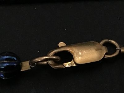 Sale Photo Thumbnail #248: Beaded strand bracelet featuring oval black beads decorated with gold-tone shamrock motifs, iridescent purple/blue accent beads, smooth black spacer beads, and brass-tone metal spacers. Fitted with a lobster claw clasp marked 'GF' (gold-filled). Measures 