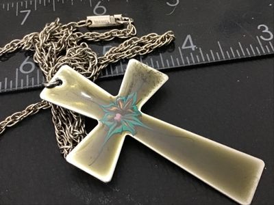Sale Photo Thumbnail #149: Vintage enamel cross pendant necklace featuring a flared cross design with hand-painted style enamel detail in turquoise, pink, and gold tones over an olive-tan background. The chain clasp is marked CELEBRITY. The pendant measures approximately 3 inches i