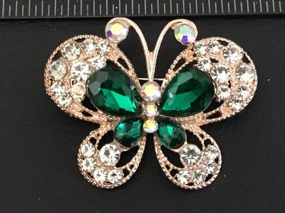 Sale Photo Thumbnail #45: A gold-tone butterfly pin/brooch featuring teardrop emerald green faceted glass stones, clear rhinestones, and iridescent aurora borealis rhinestones along the antennae and center body. Features openwork filigree details on the wings and a standard pin ba