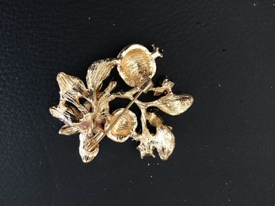 Sale Photo Thumbnail #77: Gold-tone floral brooch featuring red enamel pomegranates, green enamel leaves, a white flower, and clear rhinestone accents. Includes a standard pin back with locking clasp. In good pre-owned condition with no missing stones observed.