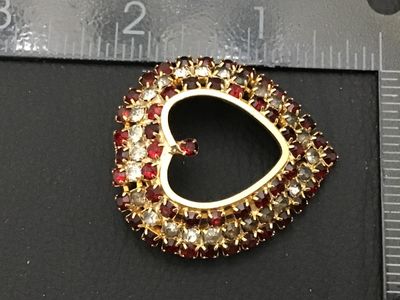 Sale Photo Thumbnail #162: A vintage gold-tone heart-shaped brooch pin encrusted with red and clear/smokey rhinestones set in prong settings. Features a rollover safety clasp on the back. Measures approximately 1.5 inches wide by 1.5 inches tall. Overall good vintage condition with