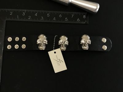 Sale Photo Thumbnail #55: Avenue Six Collection black textured leather or faux-leather cuff bracelet featuring three silver-tone metallic skulls set with clear rhinestone eyes and teeth accents. Secured with double snap closure. Measures approximately 8.5 to 9 inches long total. I
