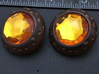 Sale Photo Thumbnail #281: Pair of vintage round clip-on earrings featuring large faceted amber-colored glass or lucite center stones set in dark brown wooden frames detailed with carved star motifs. Equipped with gold-tone clip-on backs. Each earring measures approximately 1.25 in