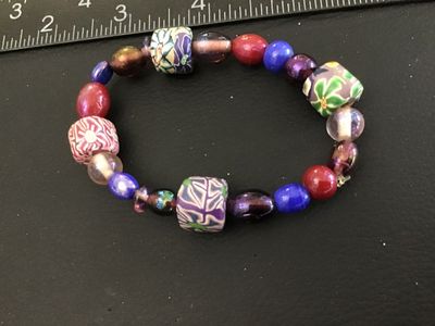 Sale Photo Thumbnail #50: Multicolor beaded stretch bracelet featuring patterned polymer clay millefiori-style focal beads alongside vibrant glass and iridescent beads in shades of purple, blue, red, and green. Measures approximately 2.5 inches in diameter resting relaxed. Good co