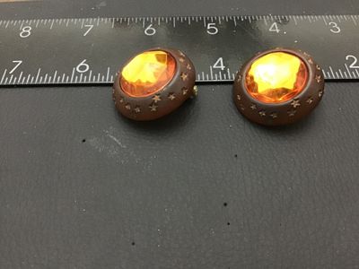Sale Photo Thumbnail #282: Pair of vintage round clip-on earrings featuring large faceted amber-colored glass or lucite center stones set in dark brown wooden frames detailed with carved star motifs. Equipped with gold-tone clip-on backs. Each earring measures approximately 1.25 in