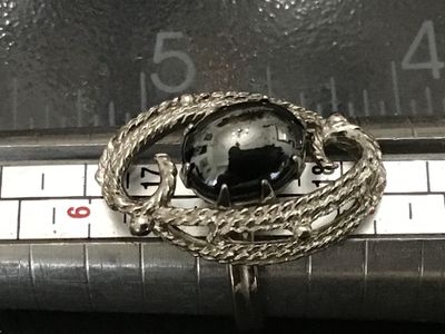 Sale Photo Thumbnail #105: Vintage Sarah Coventry silver-tone costume ring featuring a dark oval cabochon stone (hematite style) set within an ornate, textured swirl motif setting. Marked ©SARAH COV on the inner band. Features an adjustable band construction. Good vintage conditio