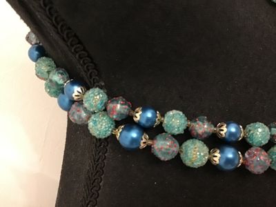 Sale Photo Thumbnail #60: A mid-century vintage double strand necklace featuring a combination of bright blue satin glass pearls, textured light blue sugar beads, and clear glass beads with red and gold foil speckles. Includes filigree metal bead caps and a decorative box clasp fe