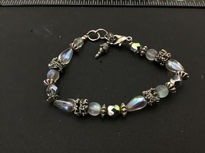 Sale Photo Thumbnail #184: Beaded bracelet featuring iridescent teardrop and faceted glass beads, frosted round beads, and ornate textured silver-tone spacer accents. Finished with a lobster claw clasp and small charm detail. In good pre-owned condition with light surface wear.