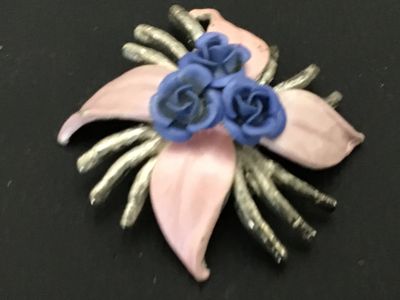 Sale Photo Thumbnail #178: Vintage silver-tone metal floral brooch featuring three blue dimensional rose buds at the center, surrounded by pale pink enamel leaves and textured silver-tone tendrils/stems. Secured with a standard rollover safety clasp on the back. Shows minor enamel 